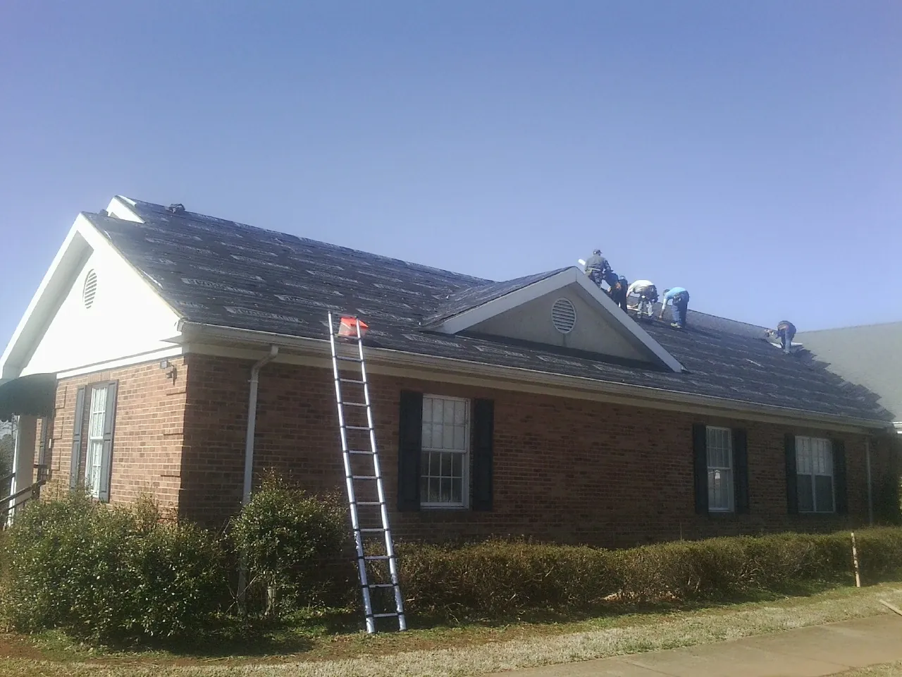 Crew tearing shingles off a brick ranch roof with a ladder set — Emergency Roof Repair work by our crew in Northampton