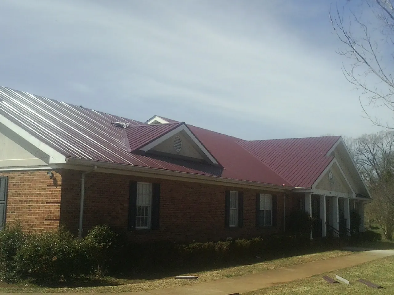 Red metal roof with gabled entries on a long brick building, from a Hail Damage Roof Repair job in Northampton