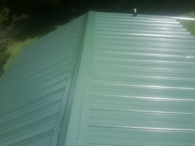 New green metal panels meeting at the ridge of a roof — Flat Roof Repair work by our crew in Northampton