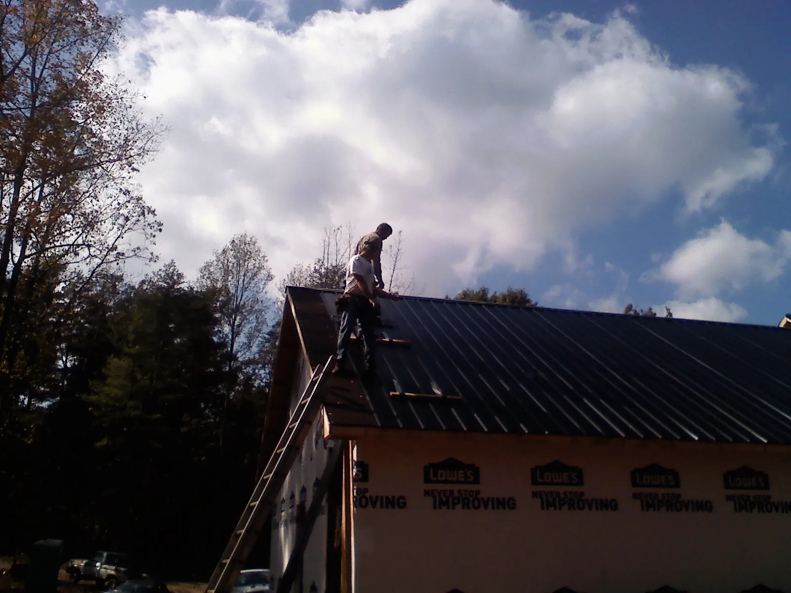 Roofer fastening dark metal panels high against a cloudy sky, from a Roof Inspection job in Northampton